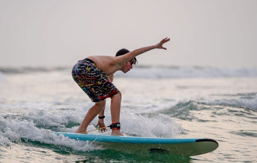 Surfer riding a wave along the tropical coast of Sri Lanka with palm trees in the background.