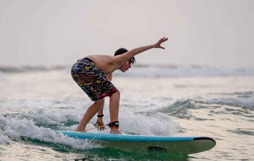 Surfer riding a wave along the tropical coast of Sri Lanka with palm trees in the background.