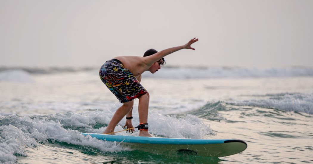 Surfer riding a wave along the tropical coast of Sri Lanka with palm trees in the background.